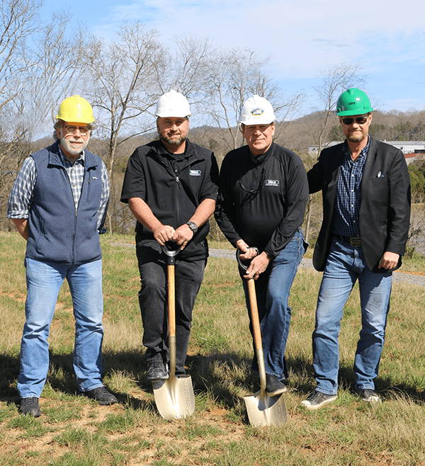 four men standing outside with hard hats and shovels